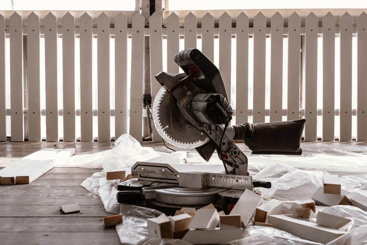 A circular saw rests on a wooden terrace with cut wood pieces and a white fence, highlighting deck construction.