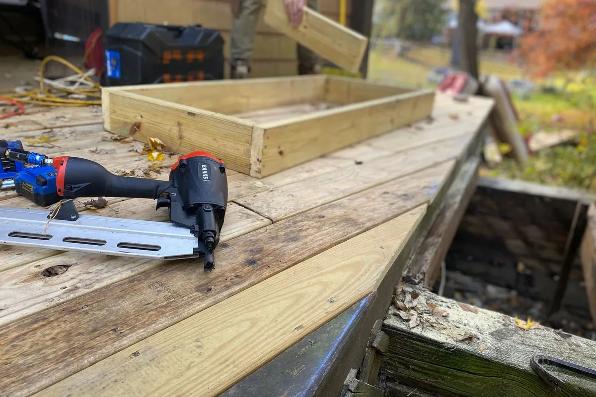 Close-up of carpentry work on a deck with a nail gun and wooden frame under construction.
