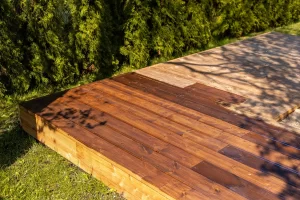 Partially stained wooden deck in a backyard with sunlight casting shadows, highlighting deck design choices.