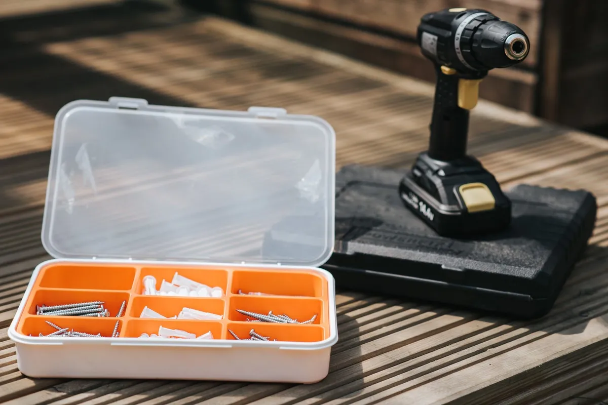 Cordless electric screwdriver on a wooden surface with screws and nails, highlighting deck repair tools.