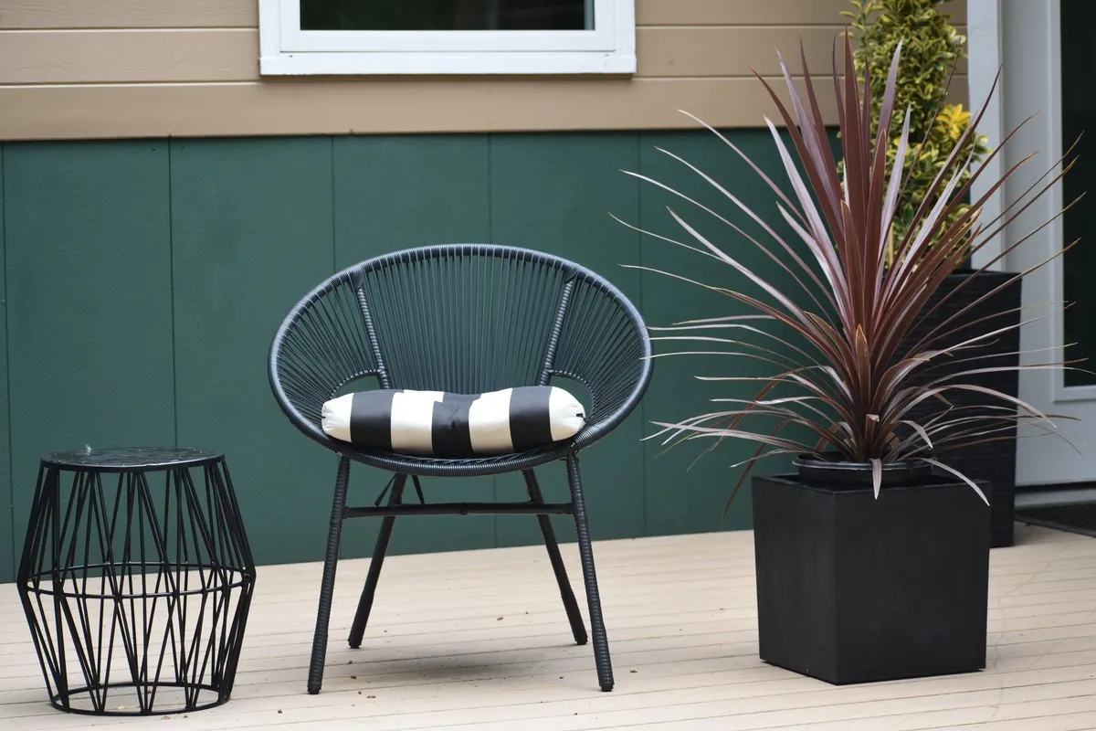 A modern outdoor patio featuring a unique chair, side table, and potted plant, ideal for deck repair inspiration.