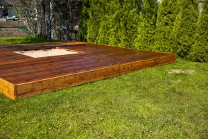 A freshly stained wooden deck with a sandpit surrounded by trees, highlighting the importance of deck maintenance.