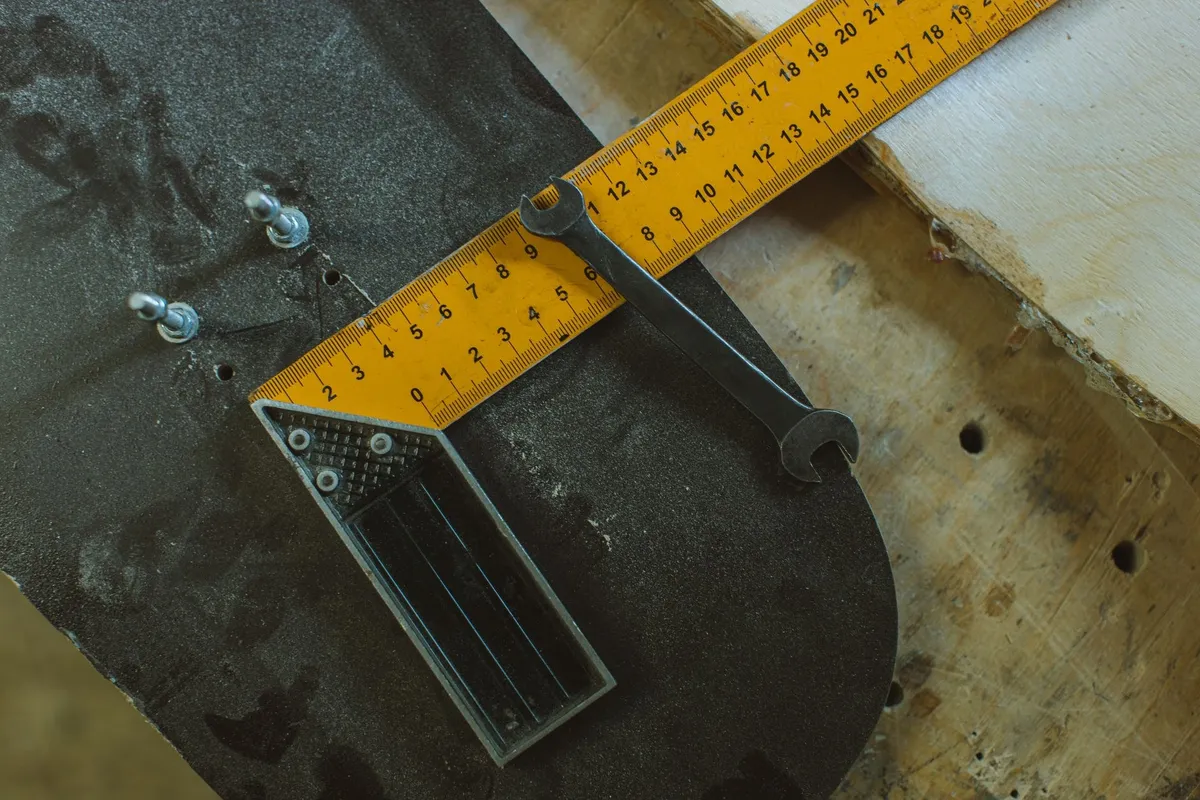 Close-up of skateboard assembly tools like a ruler and wrench on a wooden workbench, suggesting DIY repairs.